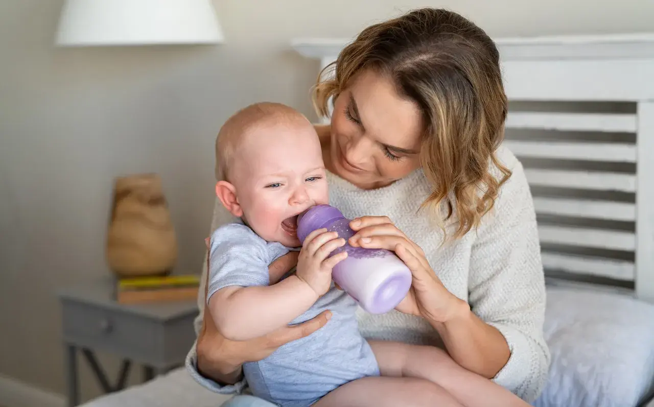 Mama karmi płaczącego malucha butelką. To może być trudny skok rozwojowy, kiedy dziecko jest marudne.